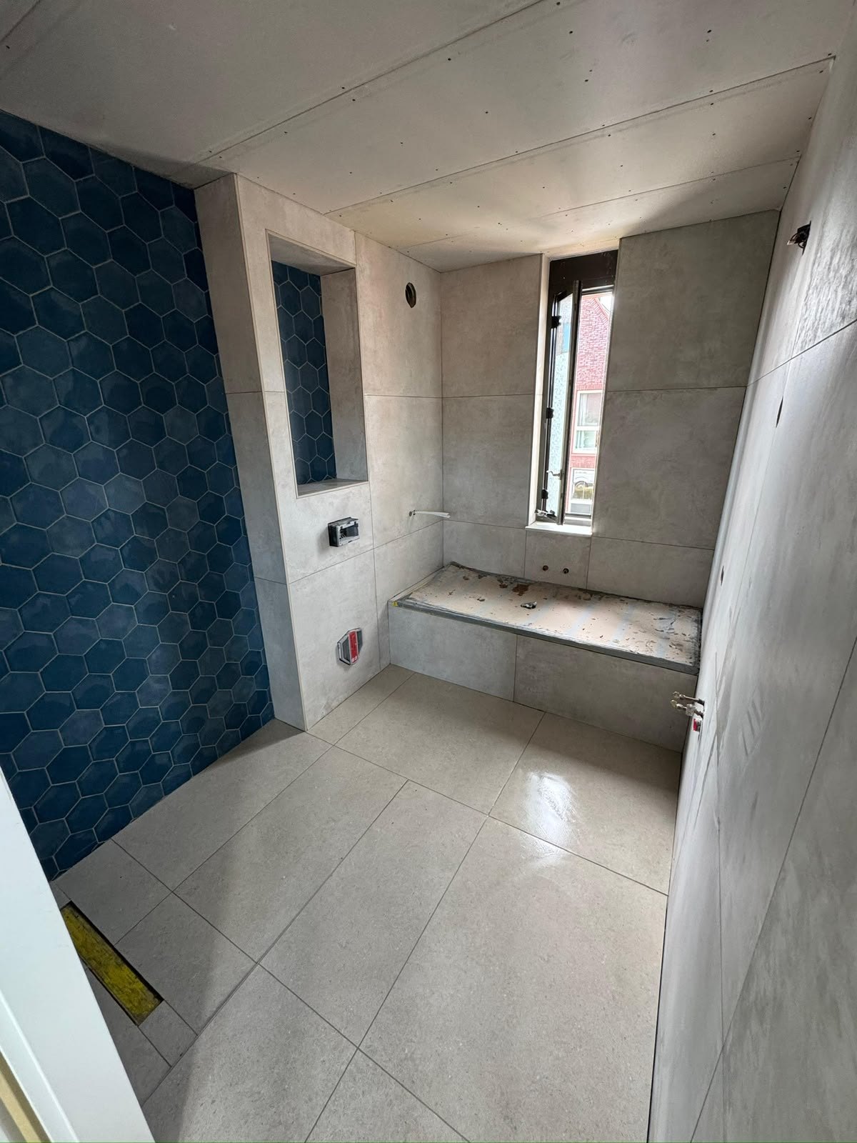 Tijdens: lichte tegels en blauwe douchewand, nog zonder sanitair