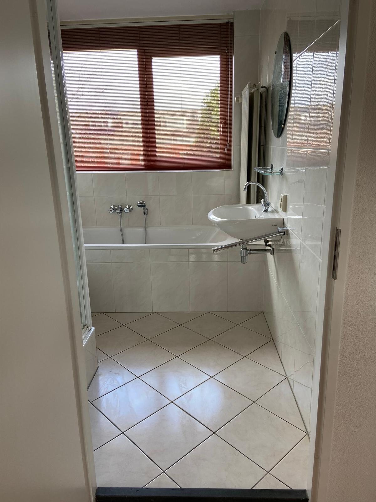 Vóór: badkamer met bad, losse douchecabine en witte tegels